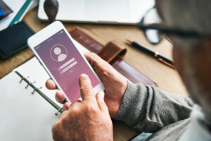 Homem acessando uma conta de login no celular em um ambiente de escritório com mesa de madeira, caneta e carteira ao redor.