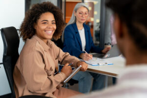 Reunião feminina de negócios com duas mulheres sorrindo em uma sala de escritório moderna.